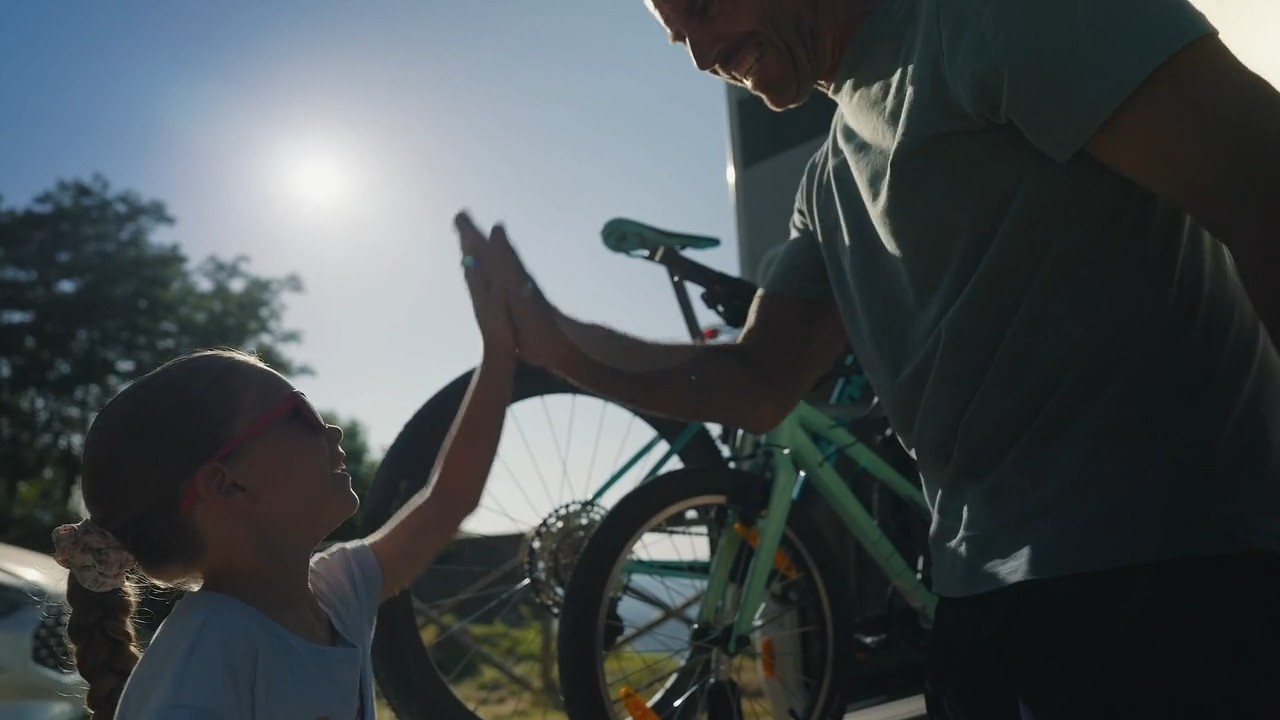 Padre e figlia si battono il cinque accanto alle biciclette: fotogramma del video di apertura di TEAM99